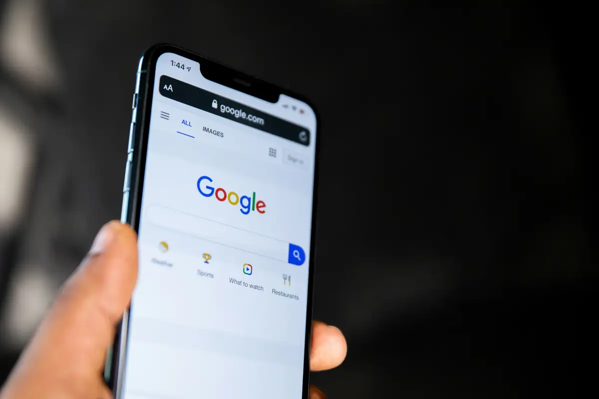 A hand holding a smartphone that shows the Google search page