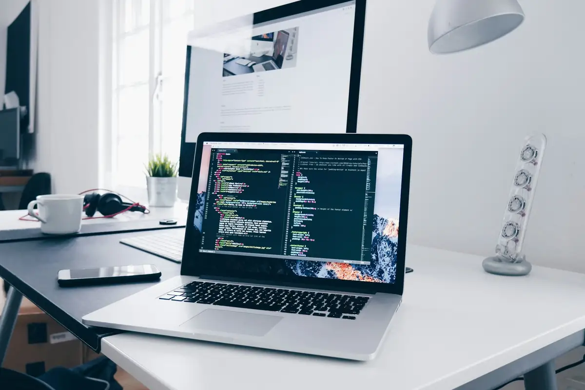 Laptop showing lines of code on a desk beside a monitor