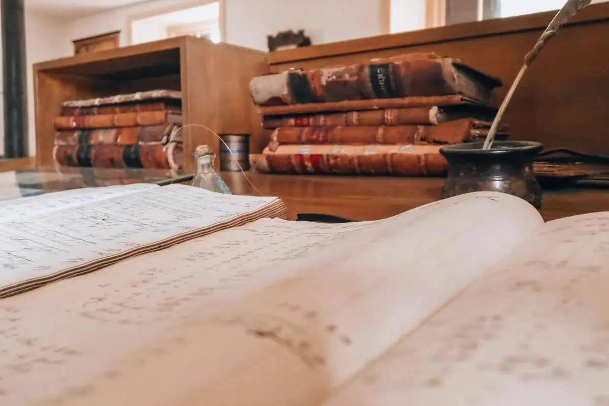 Open book and old books on a wooden desk with a quill and inkwell